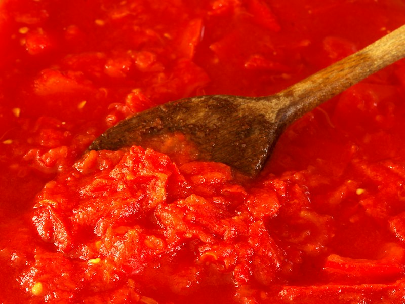 Tomato sauce being stirred with a wooden spoon