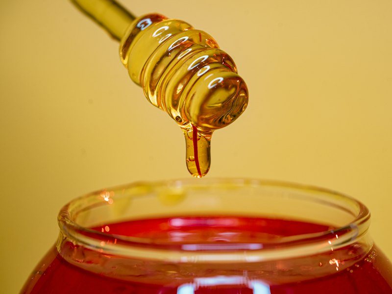 Golden honey dripping from a wooden dipper into a glass jar